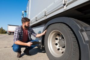 Man inspects tire on a tractor trailer.